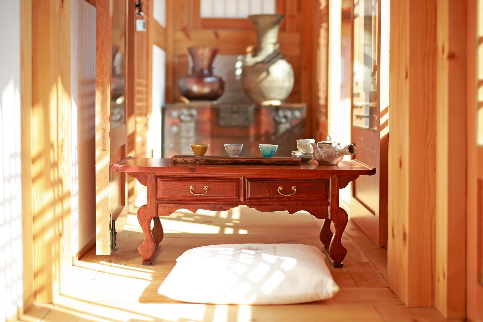 A wooden interior with a small table, drawers, and a cushion on the floor.