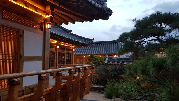 A traditional Korean-style building with wooden architecture, a wooden balcony, and a garden with pine trees. - Wiyeonjae Hanok Stay (Gyeongju)
