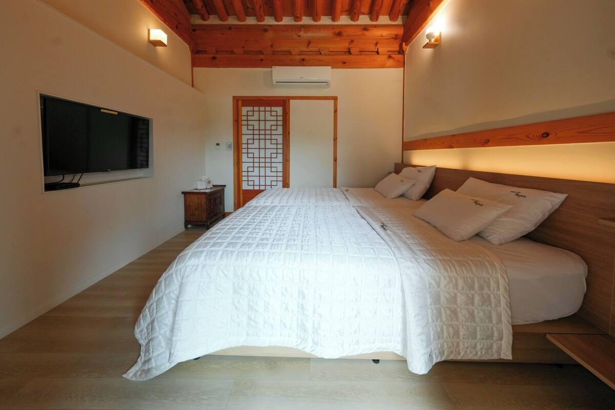 A bedroom with a bed, wooden ceiling, and a TV mounted on the wall.