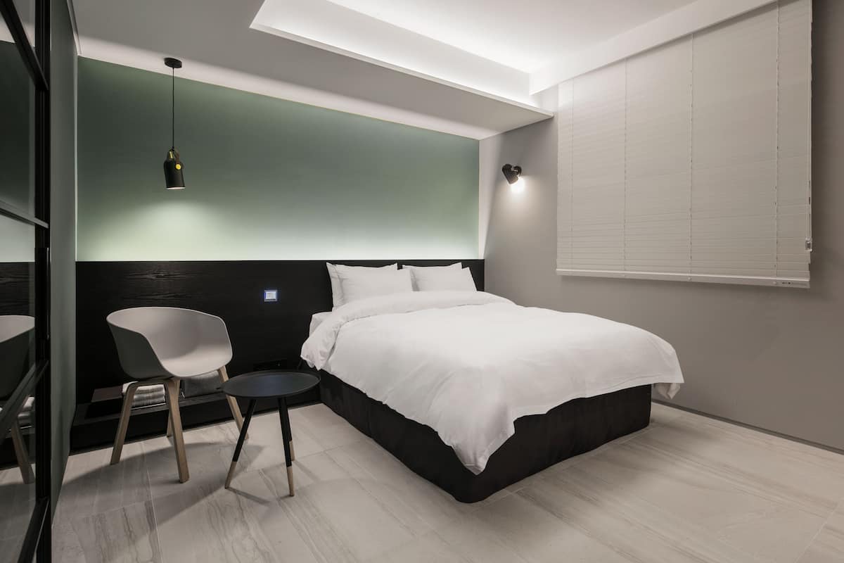 A modern bedroom with a bed, a chair, a bedside table, and a pendant light.