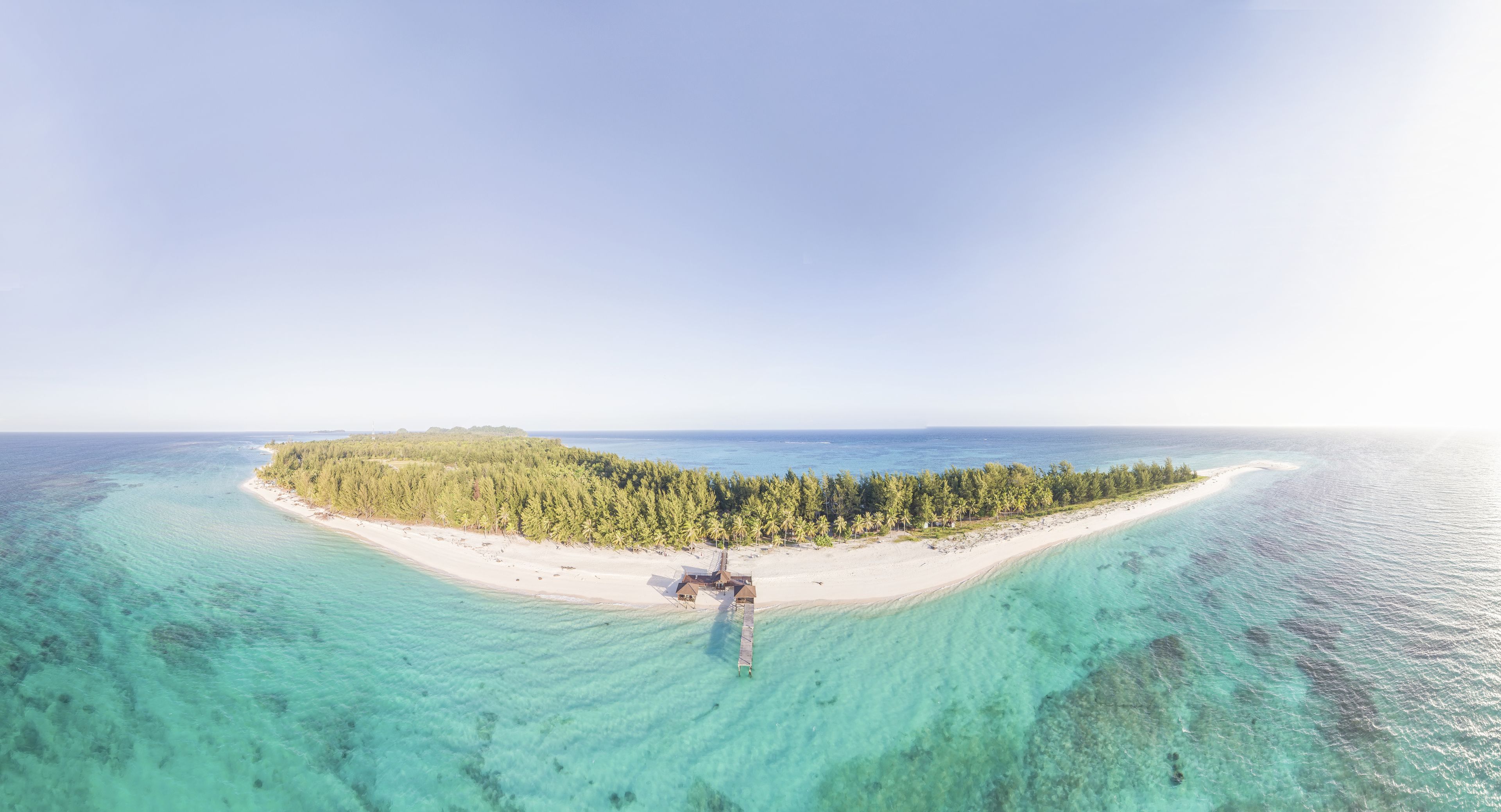 An aerial view of a tropical island with a beach, a pier, and a small building.
