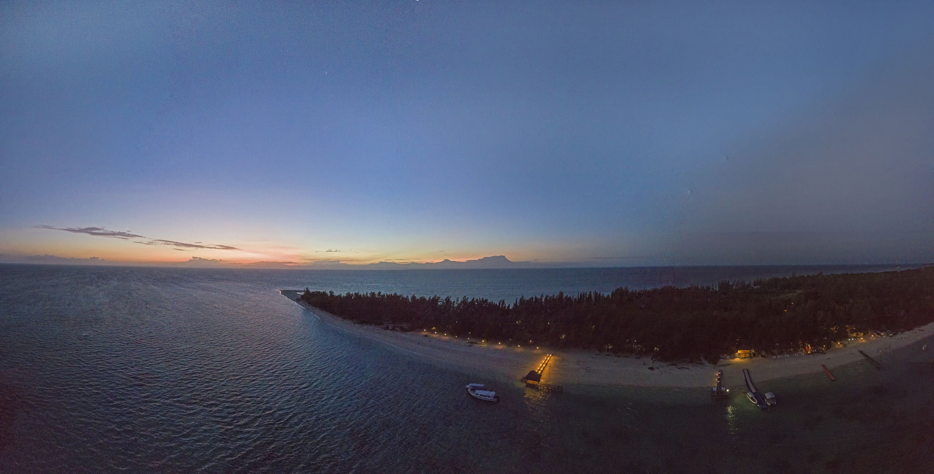 Vista aérea de una zona costera con playa, un barco y una fila de luces a lo largo de la orilla.
