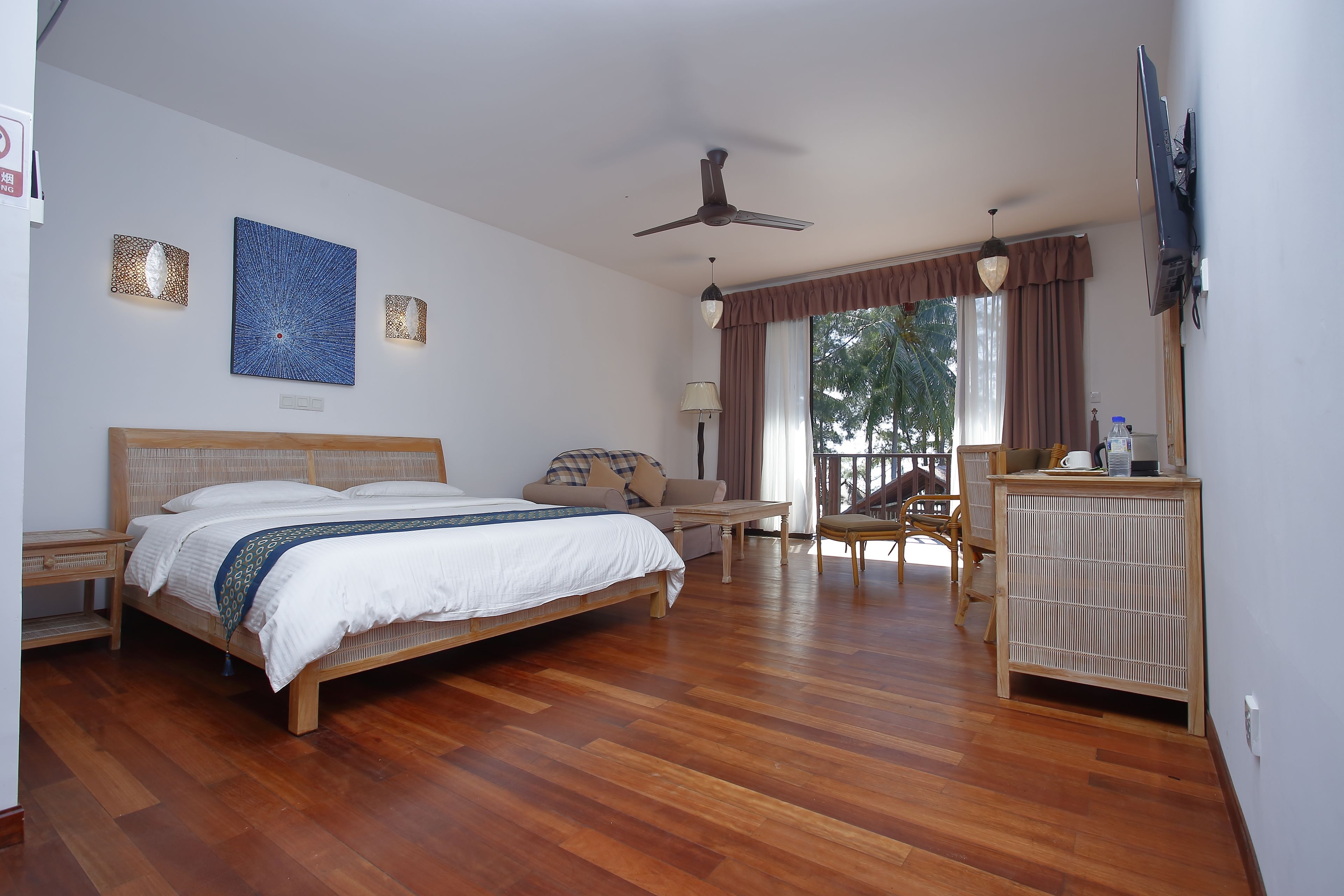 A bedroom with a wooden bed, a ceiling fan, a TV, and a view of the outdoors through a window.