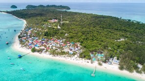 An aerial view of a tropical island with a beach, clear turquoise waters, and a small settlement with colorful buildings. - Sutera @ Mantanani Island Resort & Spa (Pulau Mantanani Besar)