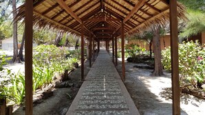 Une allée couverte, dotée d’un sol carrelé, et bordée de différentes plantes et arbres.