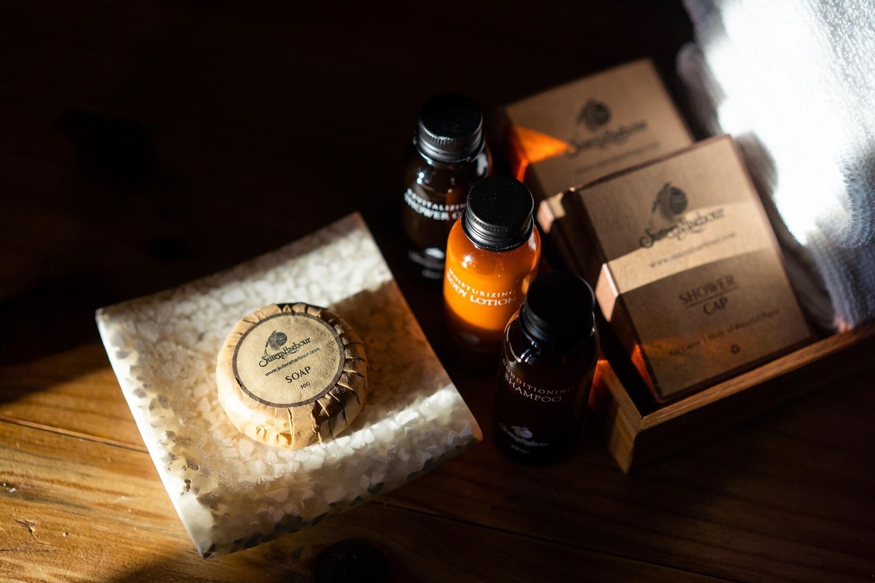 A wooden table with a bar of soap, two bottles of shampoo, and a box labeled "Shower Cap".