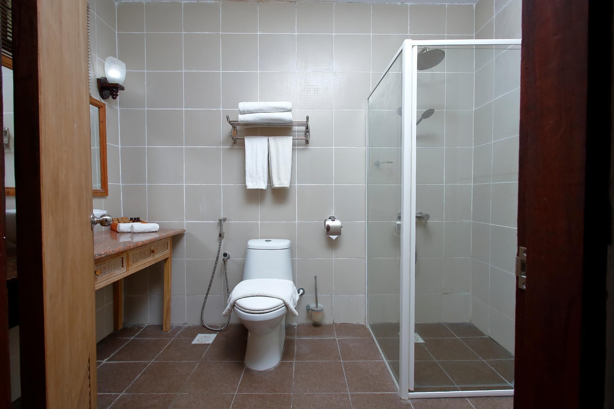 A bathroom with a toilet, a sink, a towel rack, a shower area, and a mirror.