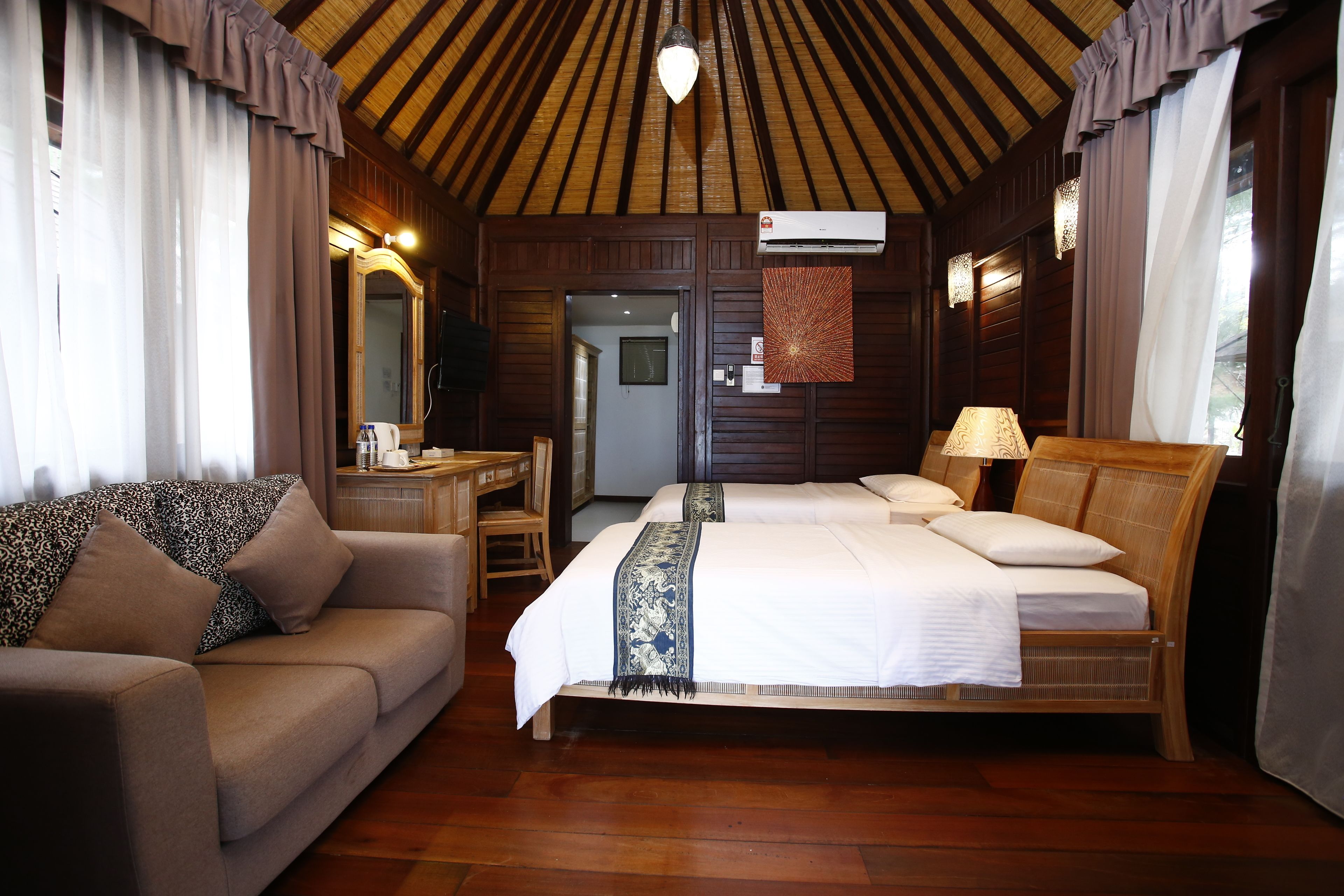 A bedroom with a wooden ceiling, two beds, a sofa, a desk, and a mirror.