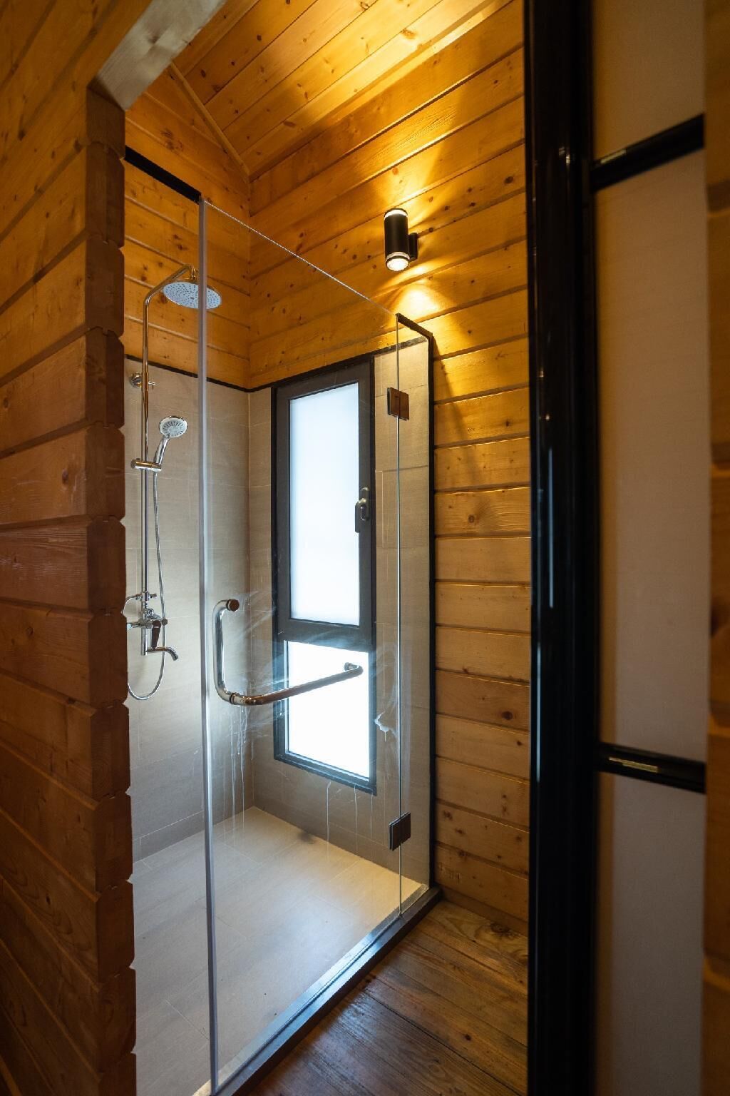Une cabane en bois dotée d’une douche à l’italienne avec des parois en verre, d’une porte visible et d’une petite fenêtre.