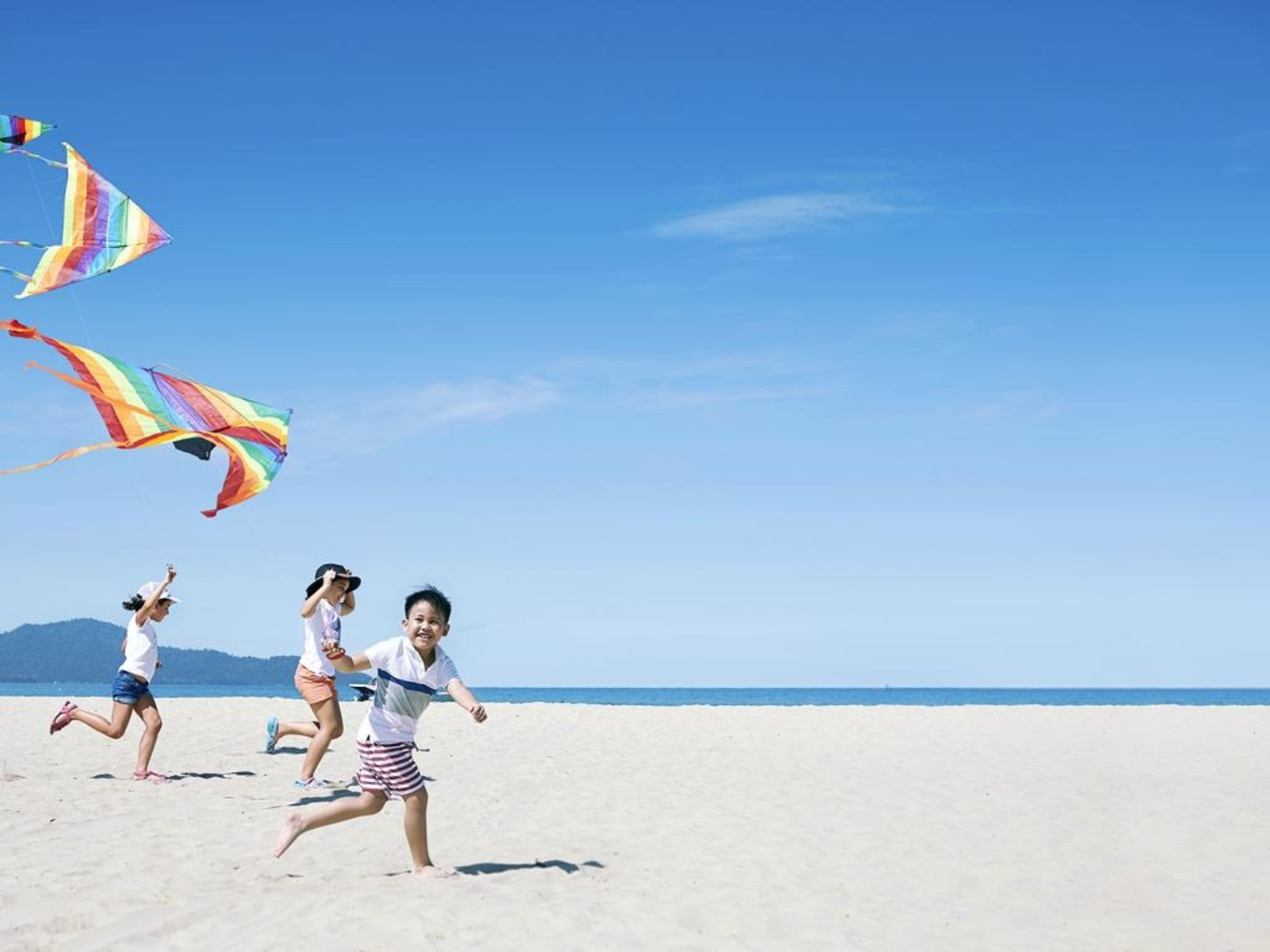 A beach scene with three people running and colorful kites flying in the sky.