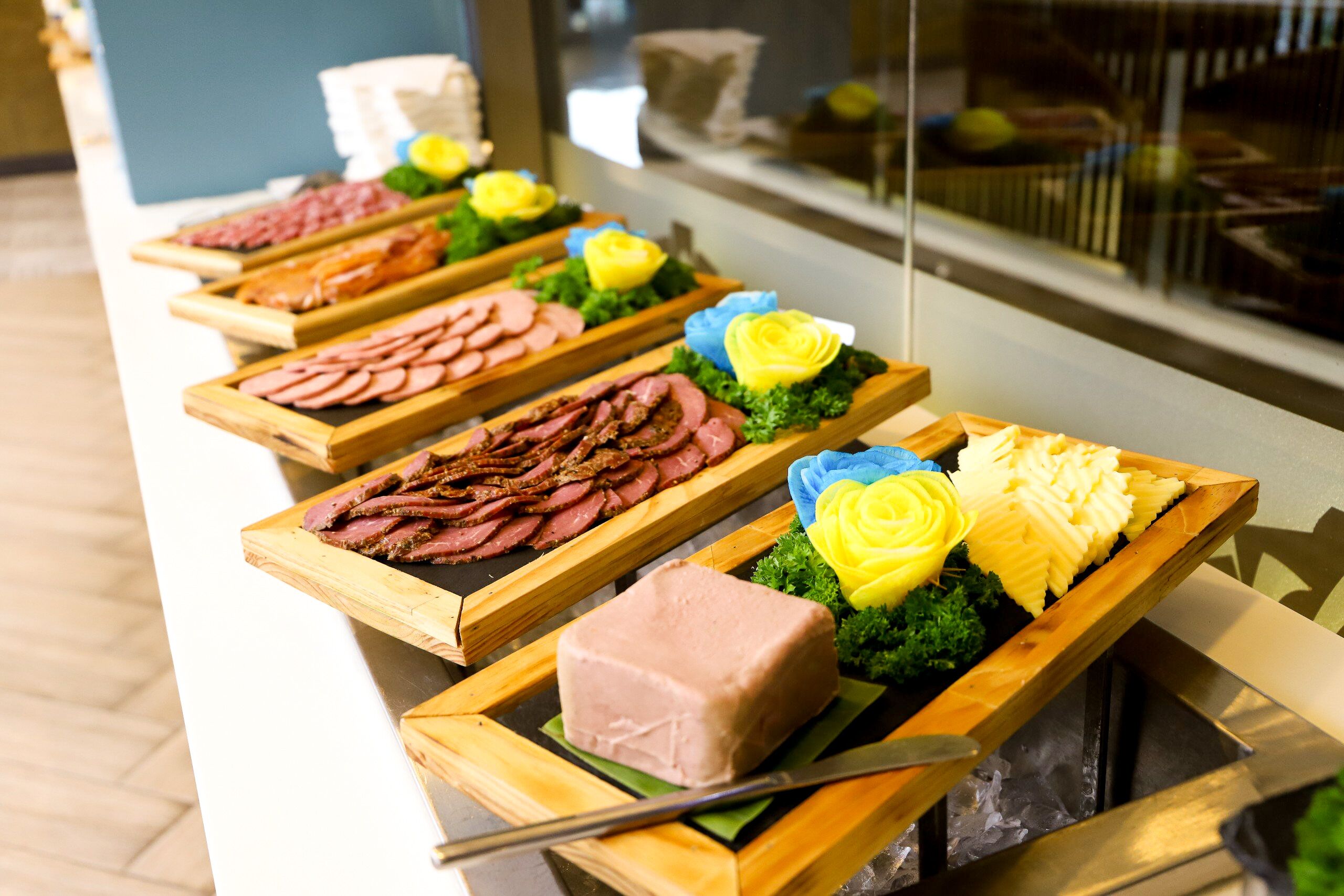 A buffet with various meat platters and a knife on a wooden board.