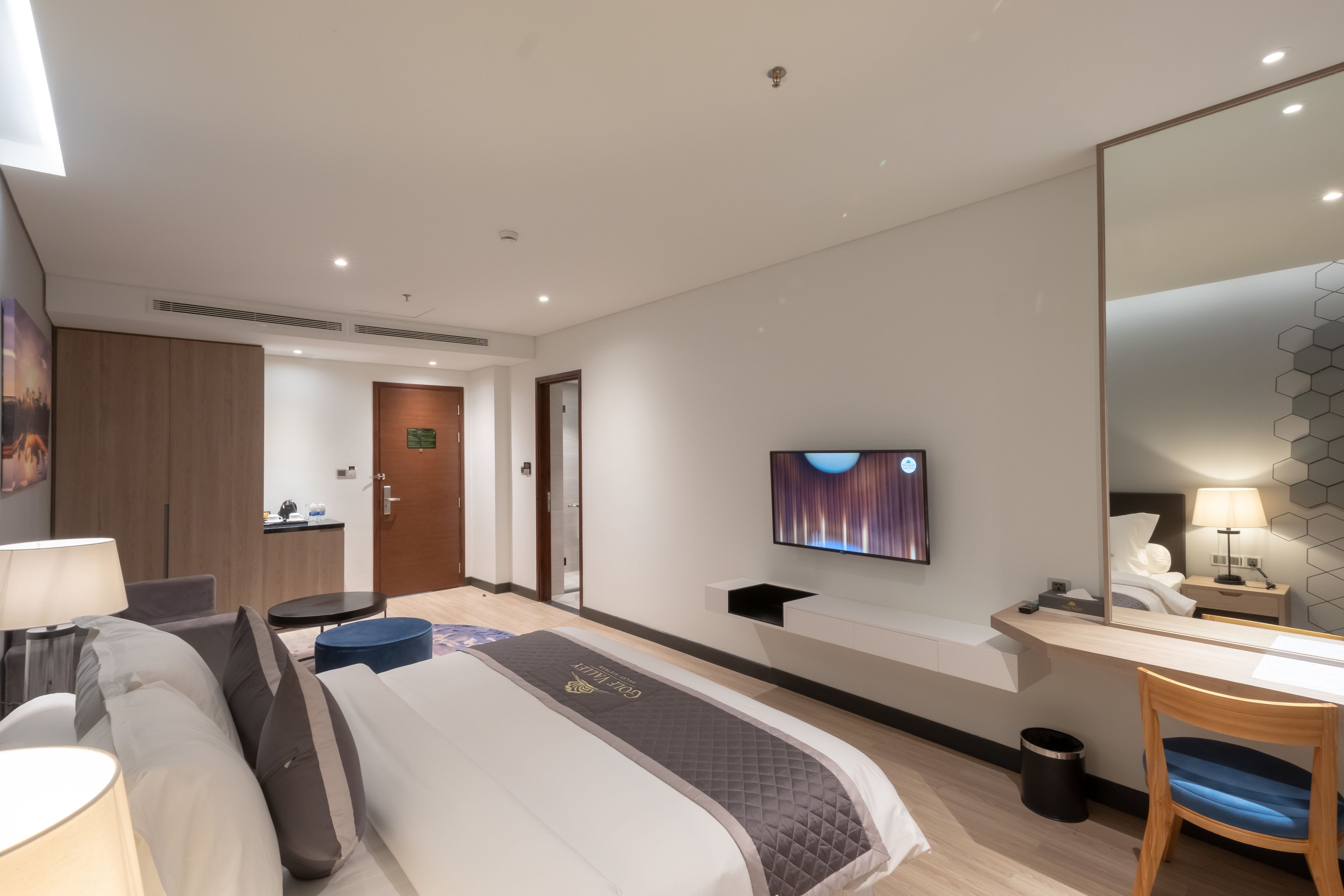 Une chambre d’hôtel moderne équipée d’un grand lit, d’une table de chevet, d’une télévision et d’un bureau avec une chaise.