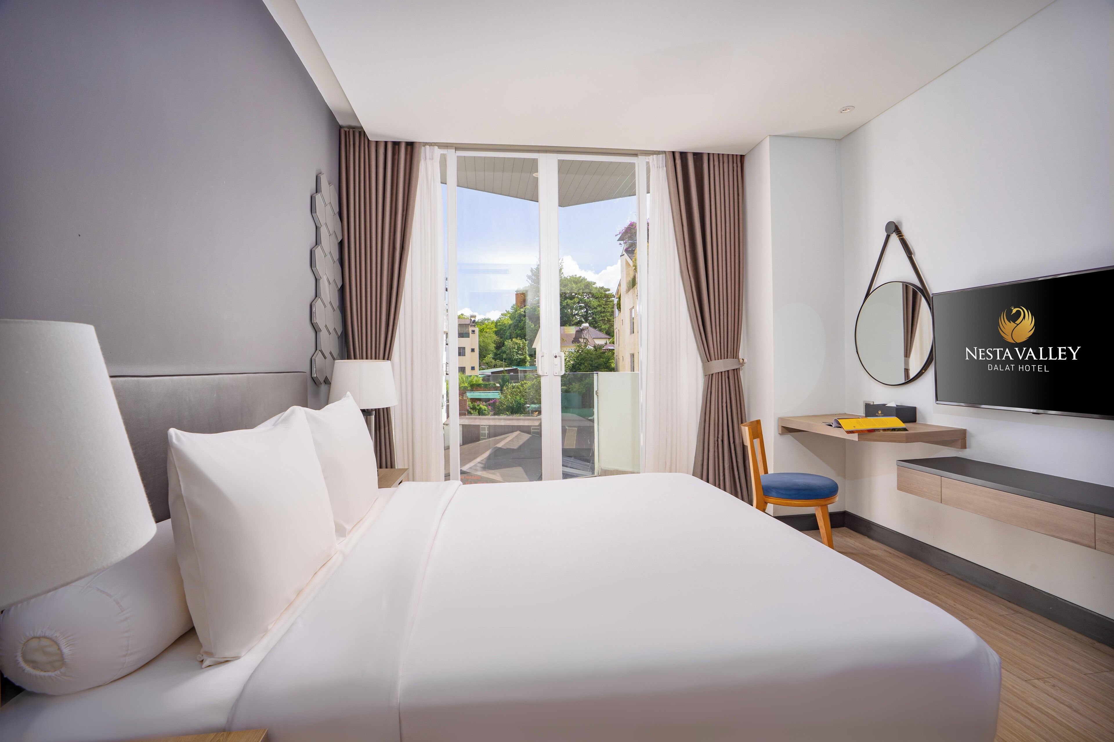 Habitación de hotel con cama, escritorio, televisor y vista al exterior.