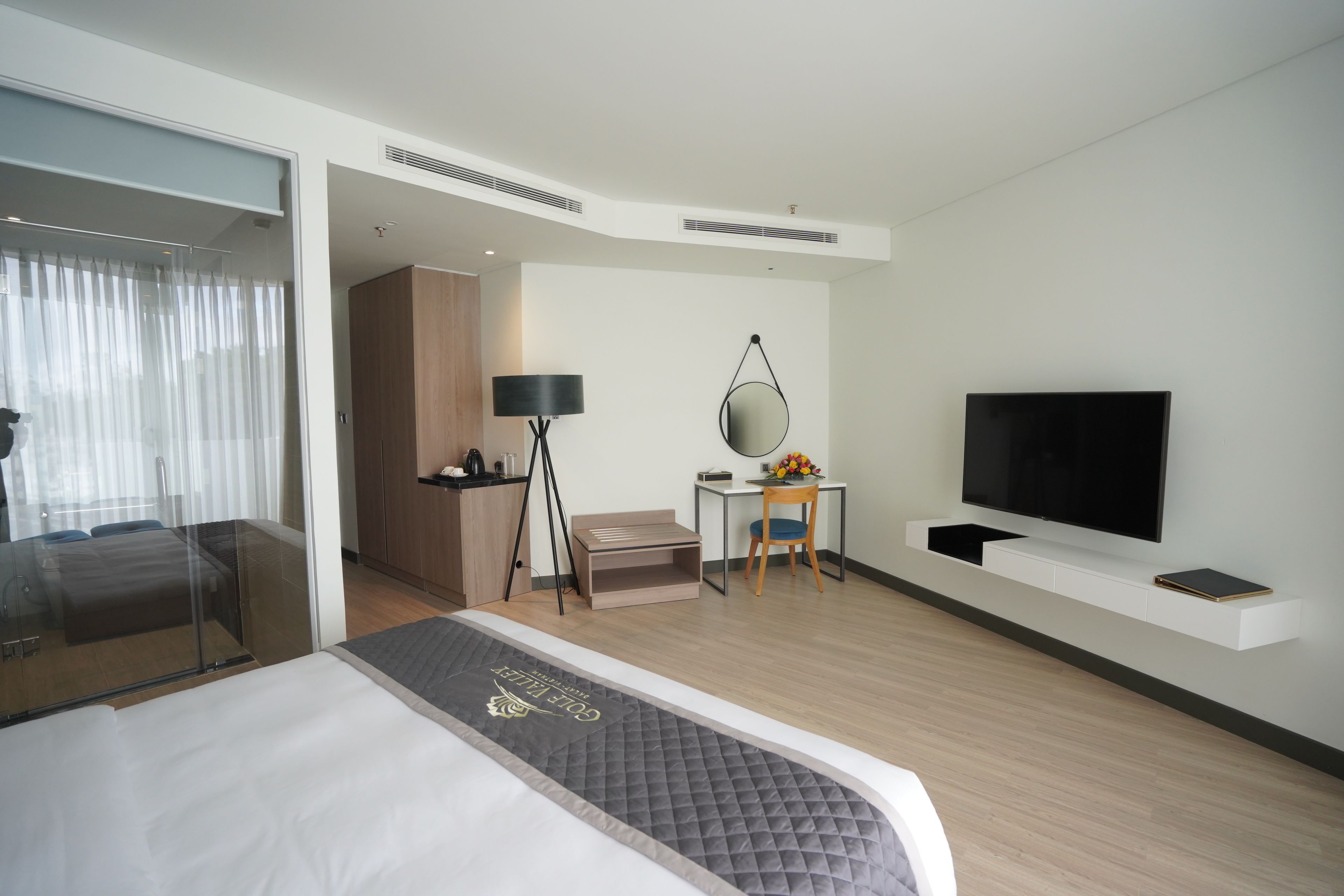 Moderni hotellihuone, jossa on sänky, työpöytä, tuoli, televisio ja suuri ikkuna, jossa on verhot.
