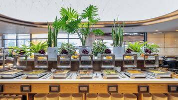 A buffet with various food stations, multiple potted plants, and stacked plates.