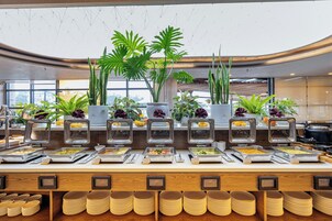 A buffet with various food stations, multiple potted plants, and stacked plates.