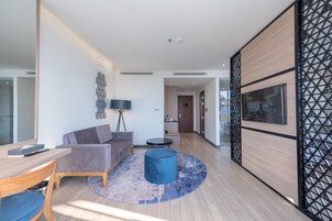 A modern living room with a sofa, a coffee table, and a TV. There is a wooden floor and a decorative wall panel.