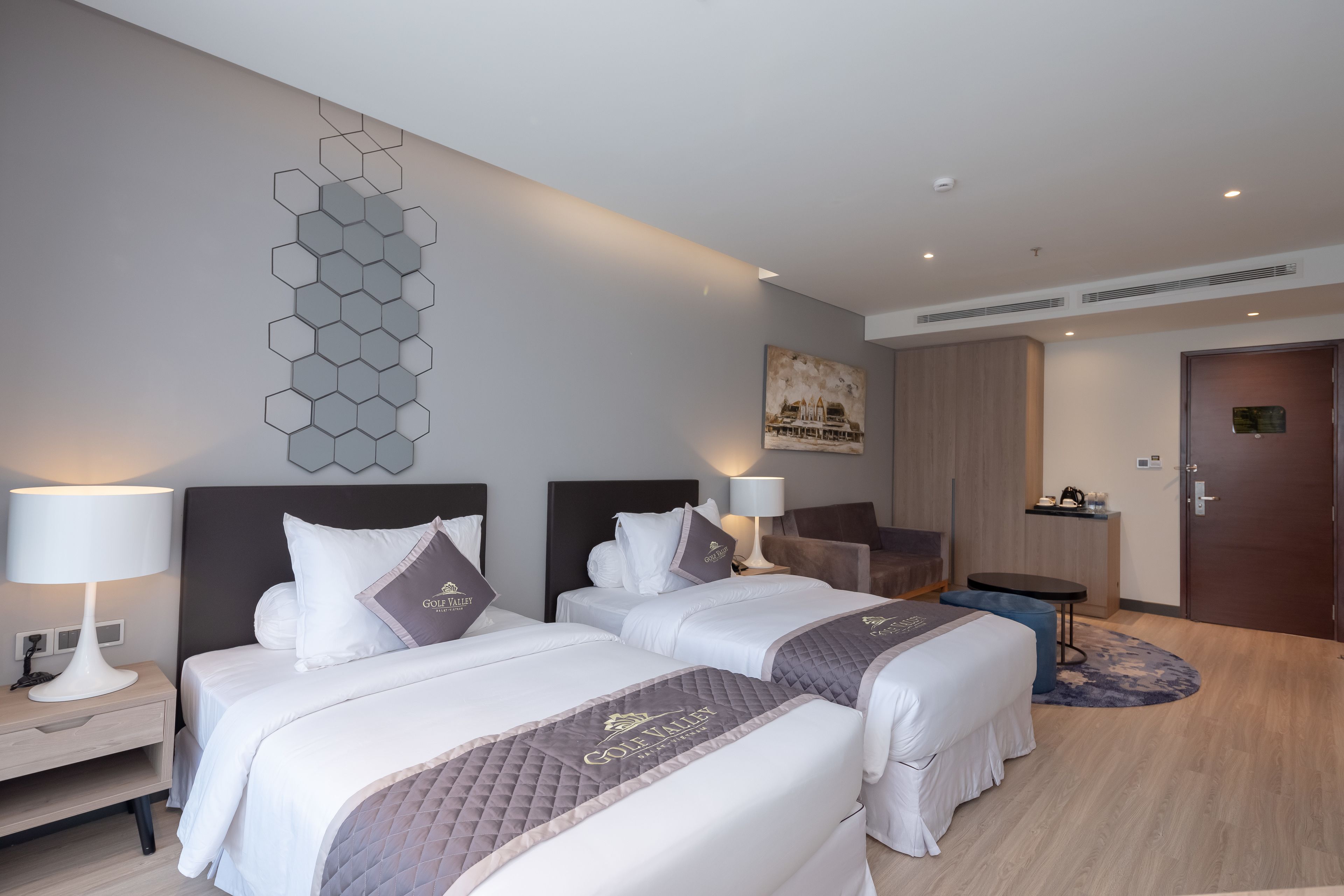 A hotel room with two beds, a desk, a chair, a small table, and a door.