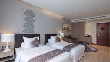 A hotel room with two beds, a desk, a chair, a small table, and a door.