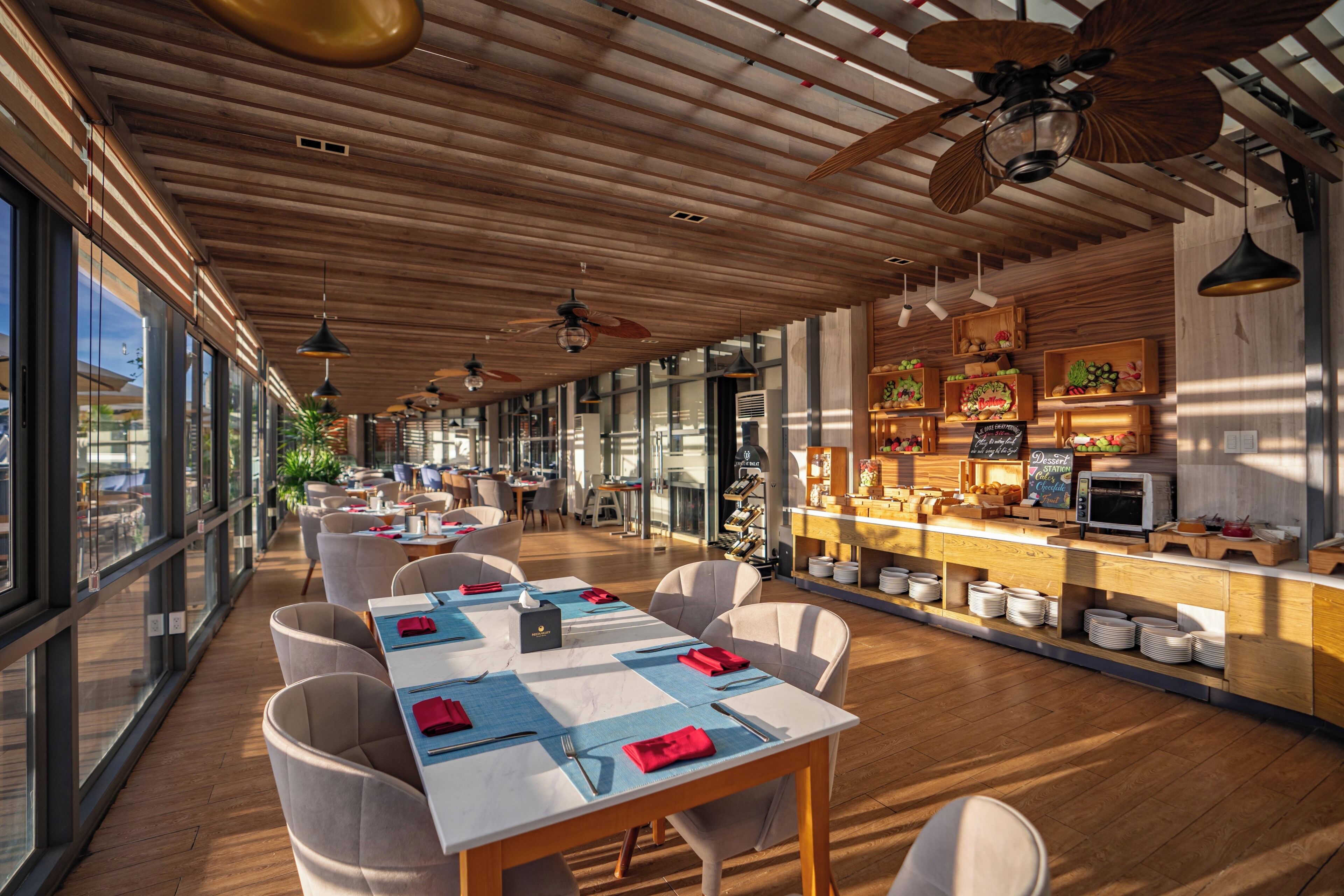 A restaurant with a long dining area, wooden ceiling, and large windows.