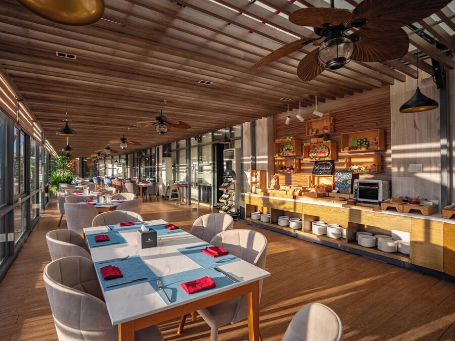A restaurant with a long dining area, wooden ceiling, and large windows.