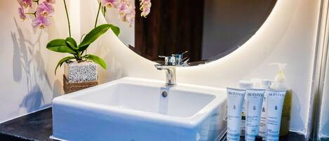 A bathroom with a white sink, a potted orchid, and toiletries on the counter.