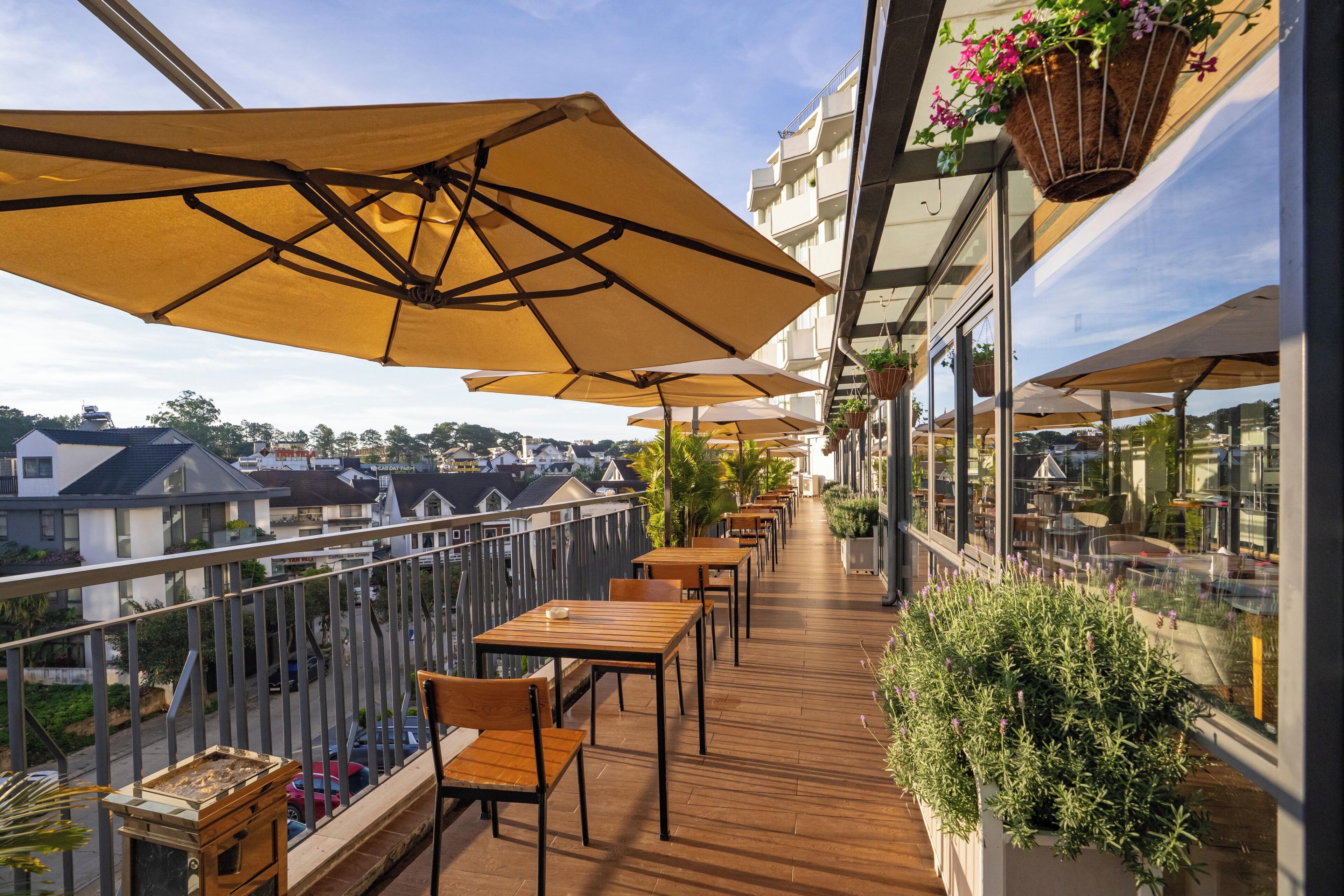 A balcony with wooden tables and chairs, large umbrellas, and hanging flower baskets.