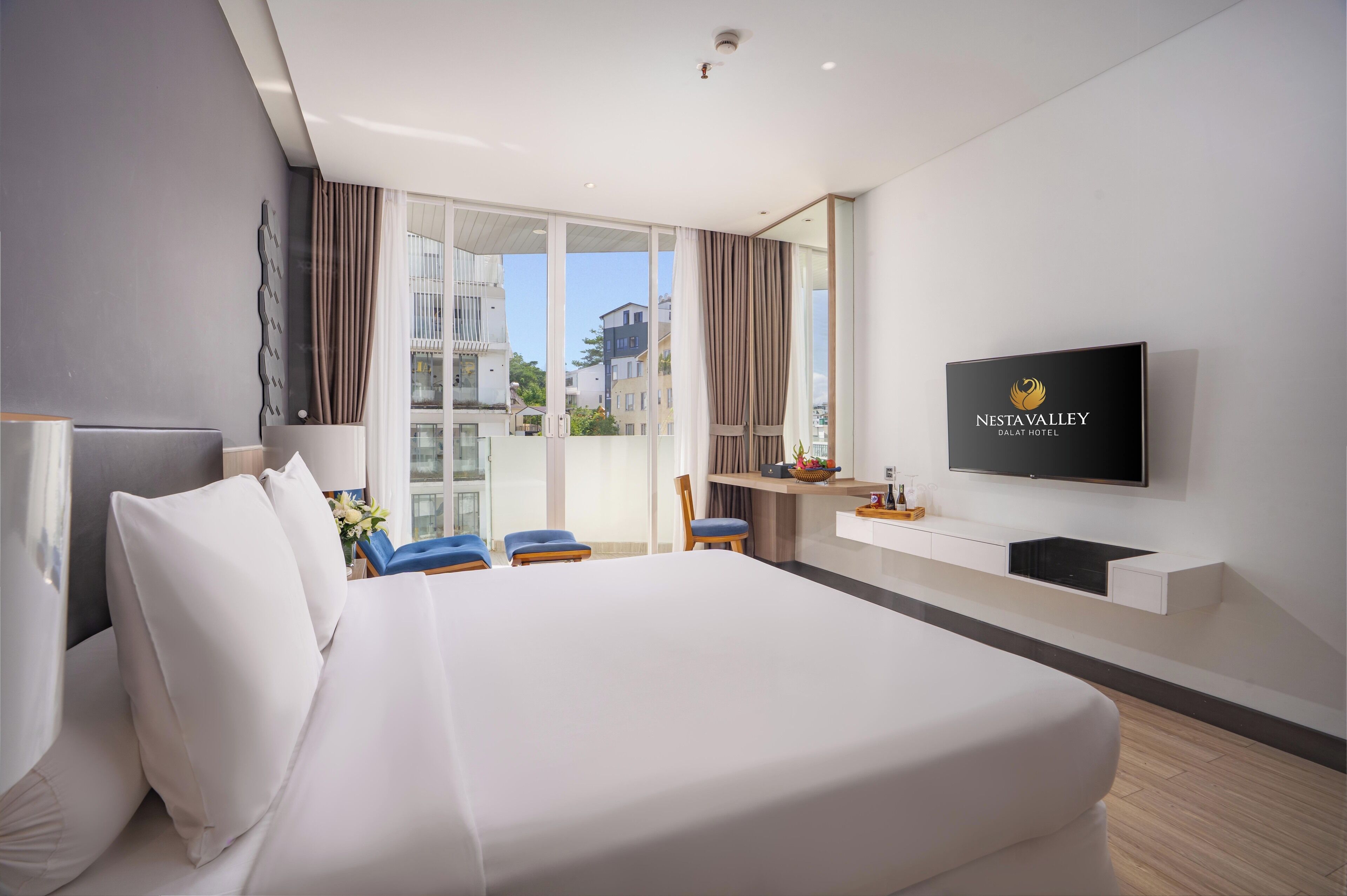 A hotel room with a large bed, a TV mounted on the wall, and a balcony with curtains.