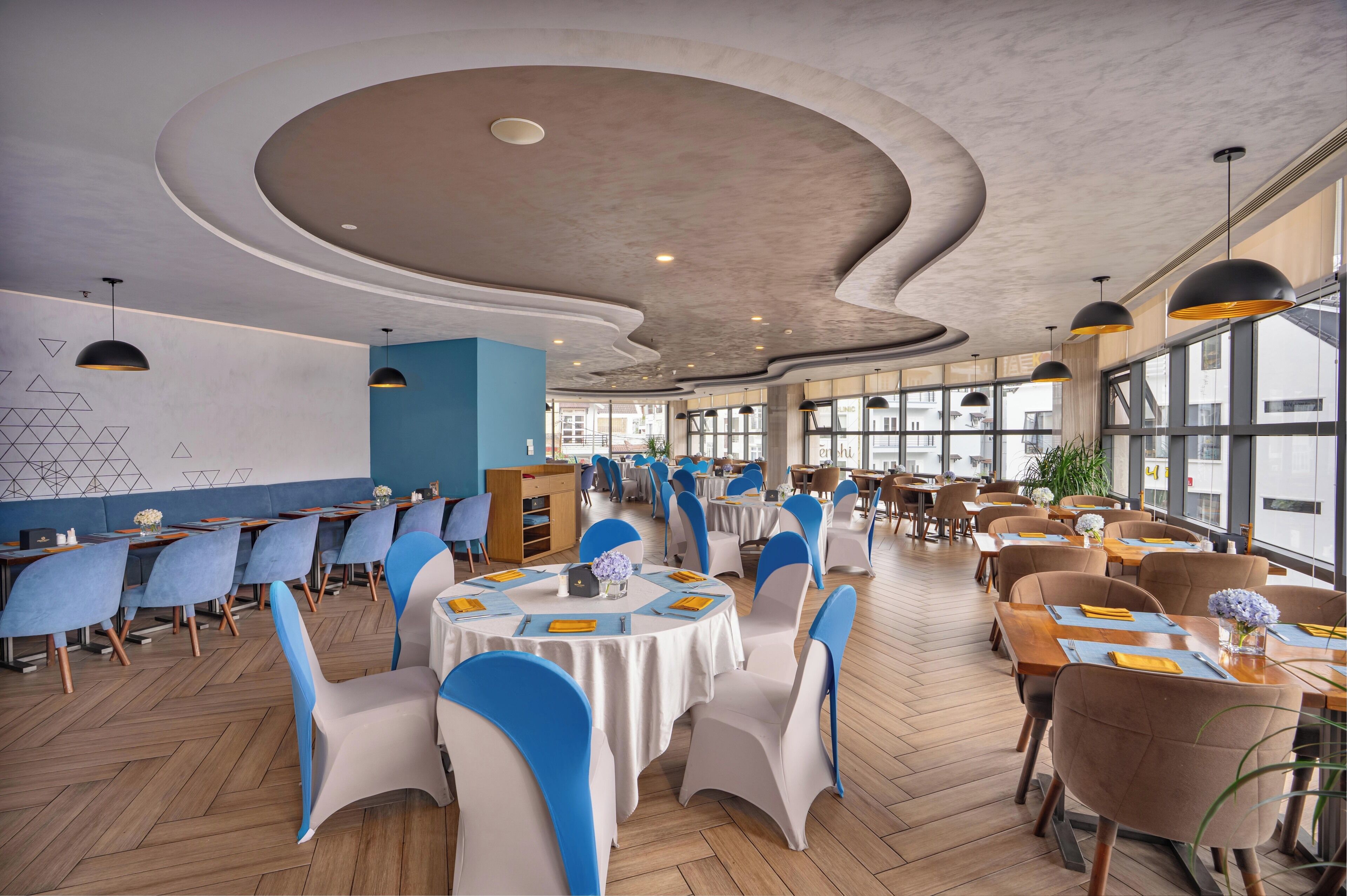 A spacious restaurant with round tables, blue and white chairs, and a modern ceiling design.