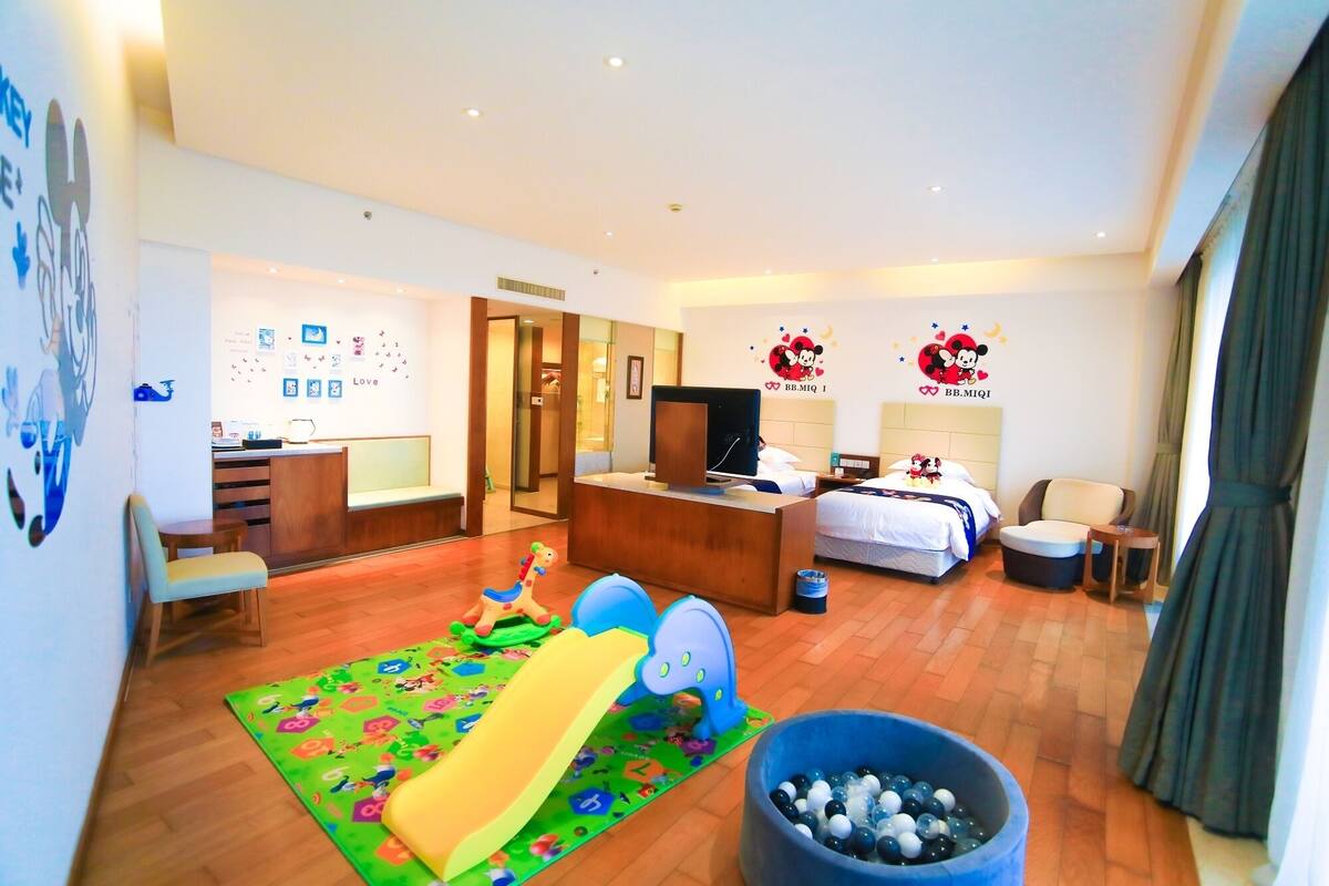 Een hotelkamer met een bed, een bureau, een televisie, een kinderspeelruimte en een groot raam.