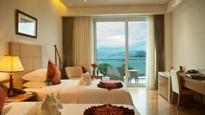 Habitación de hotel con dos camas, un escritorio, una silla, una lámpara y vistas al mar.