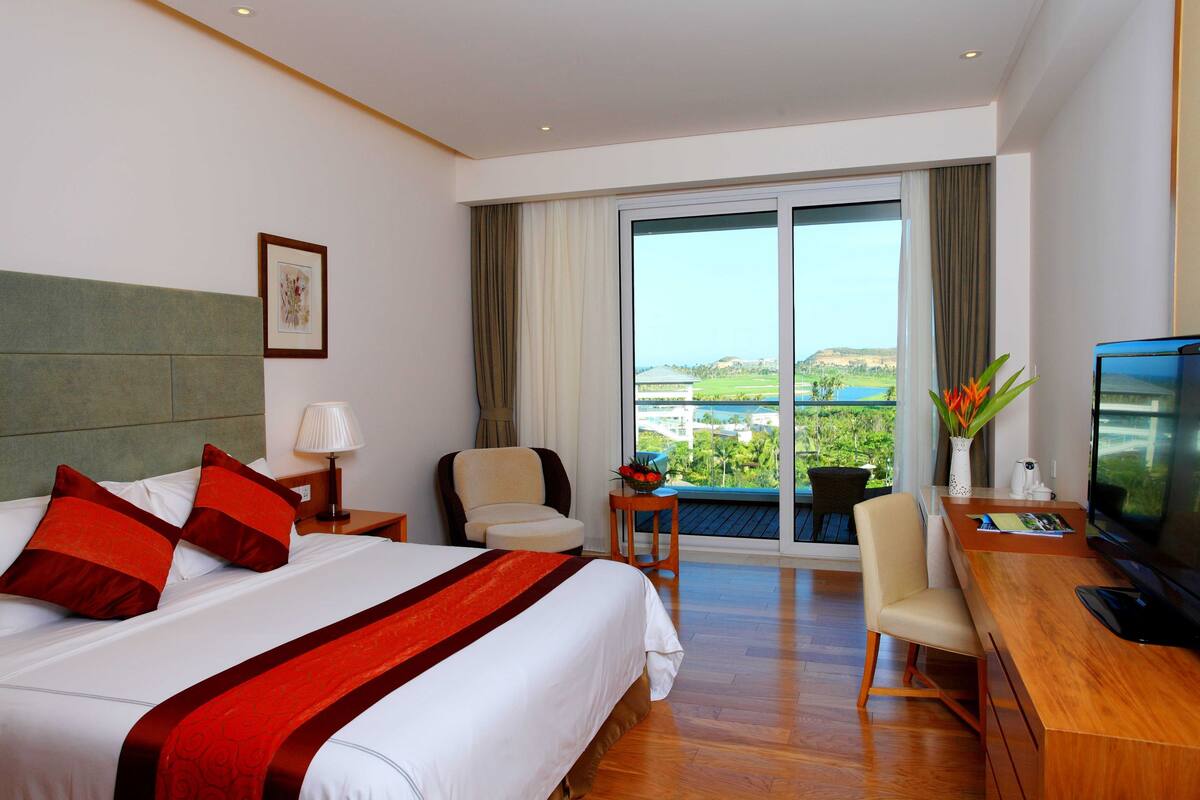 Hotelkamer met een groot bed, een bureau met televisie, een stoel en uitzicht op het omliggende landschap, met gordijnen voor het raam.
