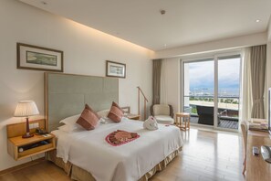 A hotel room with a large bed, a desk, a chair, a balcony with a view, and a large window.