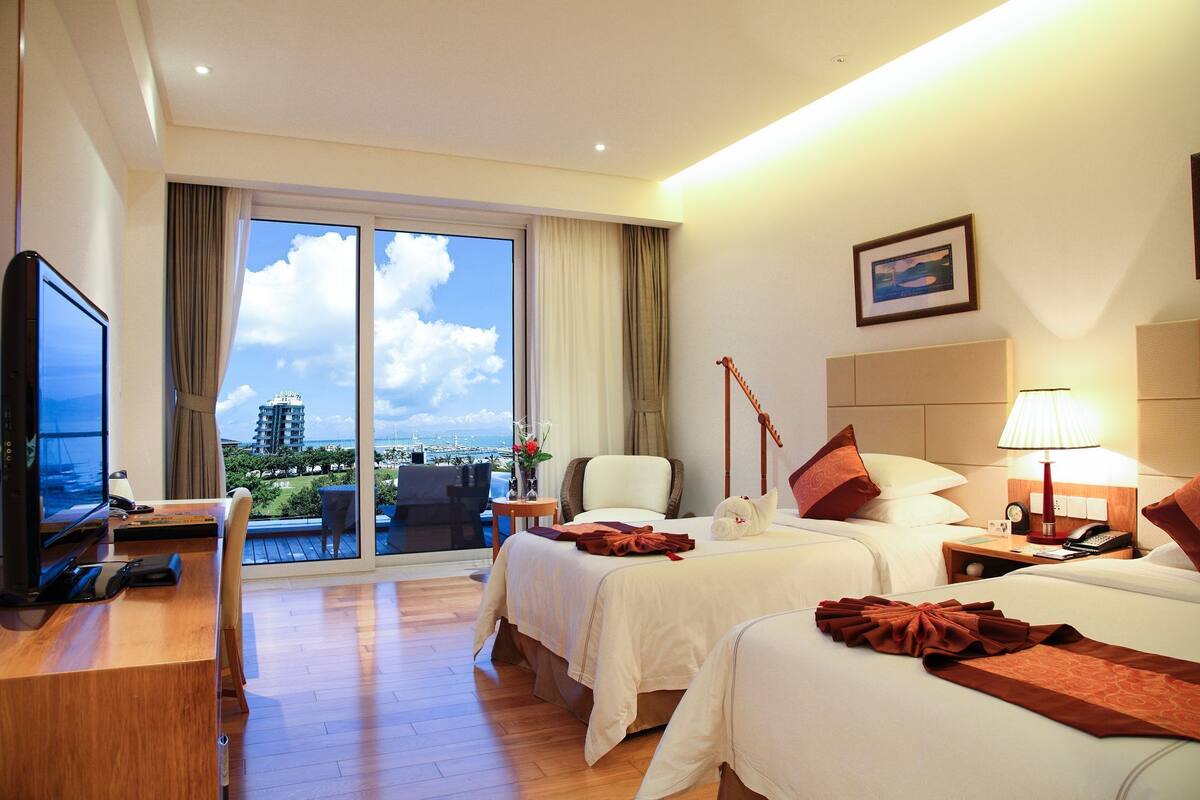 Hotelkamer met twee bedden, een bureau met een computer, een televisie en uitzicht op de stad en de jachthaven.