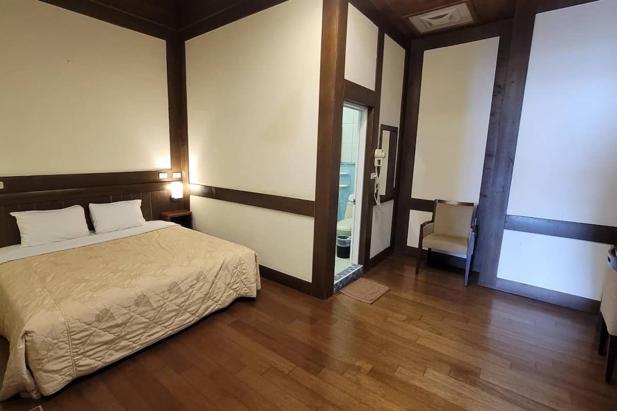 A hotel room with a large bed, wooden floor, and a small seating area.