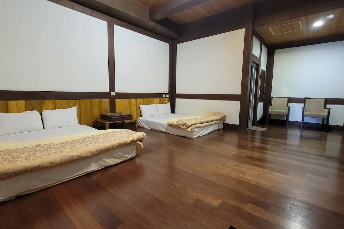 A hotel room with two beds, wooden flooring, and a small table.