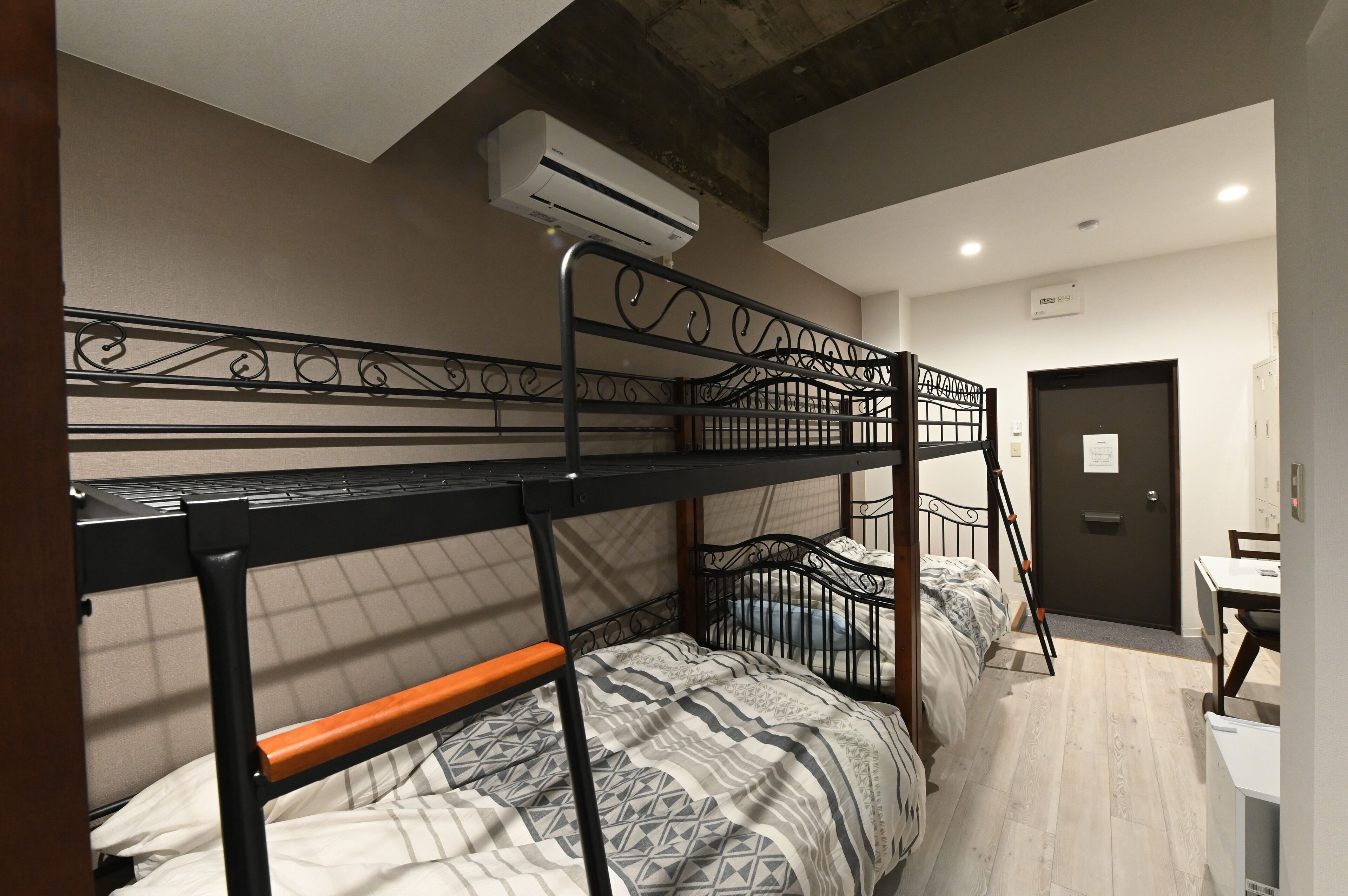 A bunk bed room with a wooden floor, a desk, and a door.