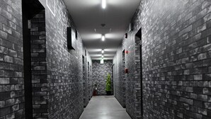 A long, narrow hallway with brick walls and a grey floor, leading to a door at the end. - Suzumaru Hotel - Hostel (Wakayama)