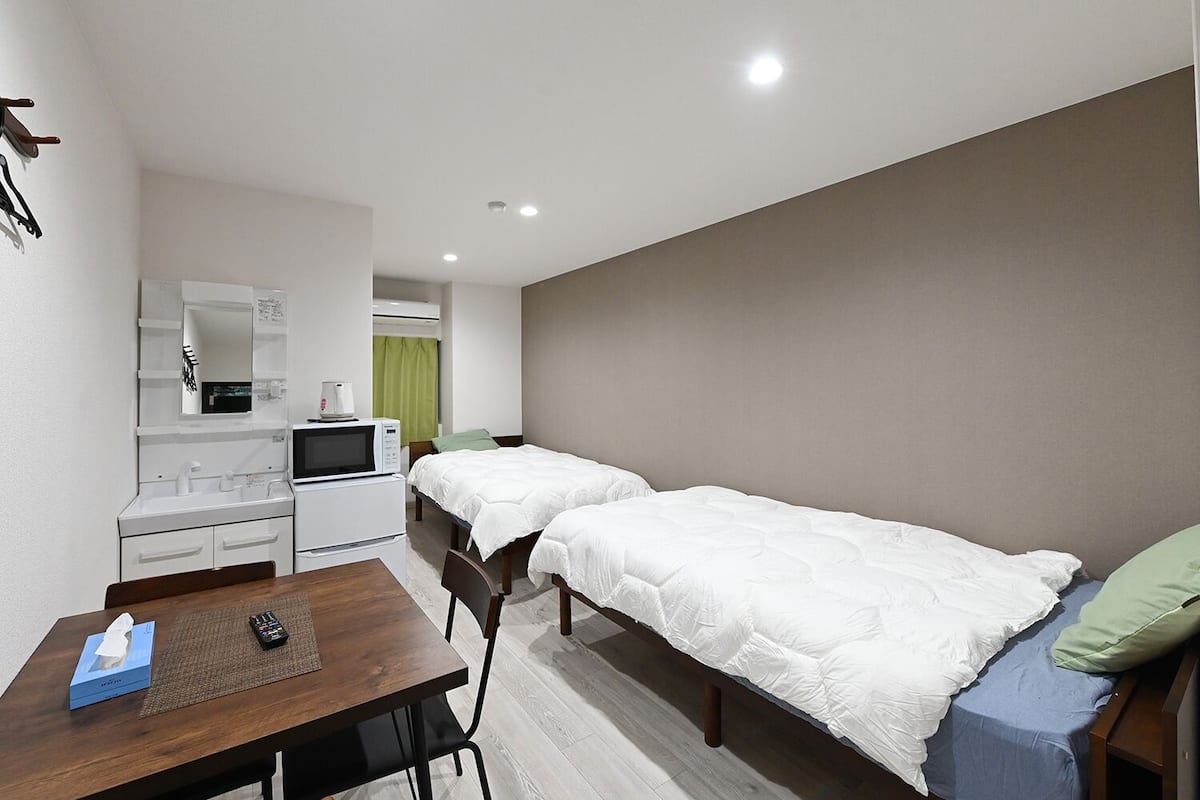A hotel room with two single beds, a small desk with a chair, a microwave, and a mini-fridge.
