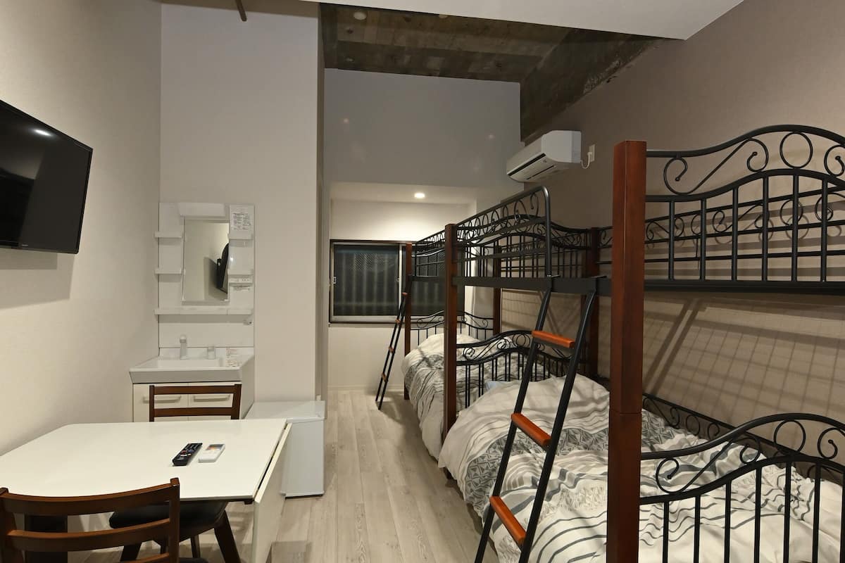 A room with bunk beds, a desk, a chair, a TV, and a mirror.