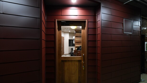 A wooden door with a small window above it, set in a wall with a red panel design. - Suzumaru Hotel - Hostel (Wakayama)