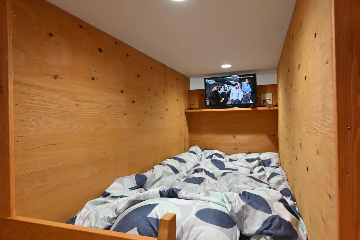 A wooden bunk bed with a television mounted above it.