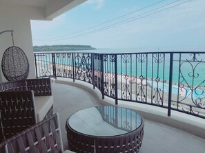 A balcony with a glass table and chairs, overlooking a beach with a clear view of the sea and distant land. - Tsuki No Michi Terrace (Motobu)