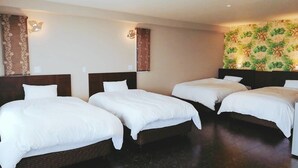 Une chambre d’hôtel avec trois lits simples, des têtes de lit en bois foncé et un papier peint à motifs floraux sur un des murs.