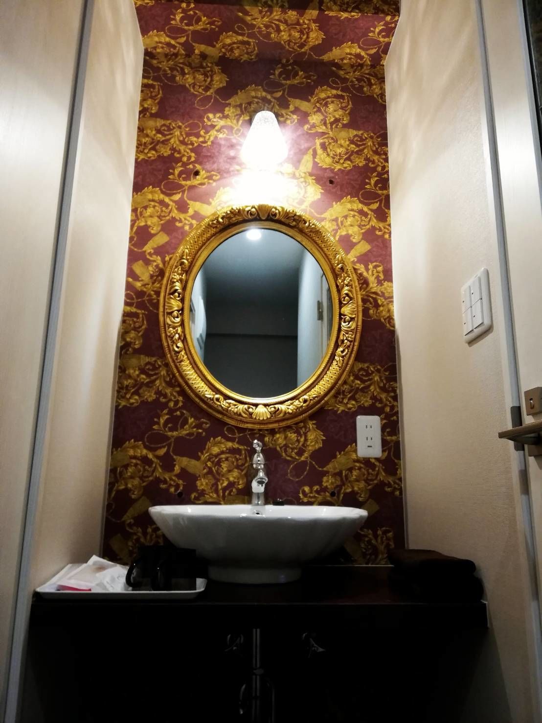 A bathroom with a gold-framed mirror, a white sink, and a dark vanity.