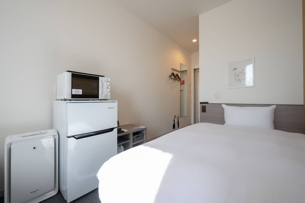 A hotel room with a bed, a refrigerator, a microwave, and a small heater.