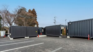 A parking lot with several large shipping containers, some with doors open, and a few trees in the background.