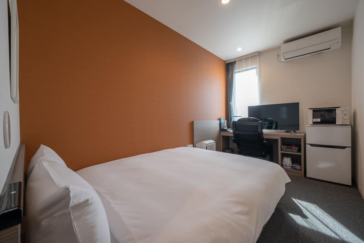 A hotel room with a bed, desk, chair, television, and a refrigerator.