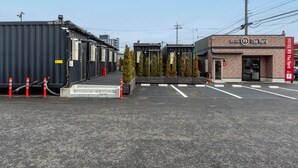 A hotel with a brick facade, a parking lot, and shipping containers in the background.