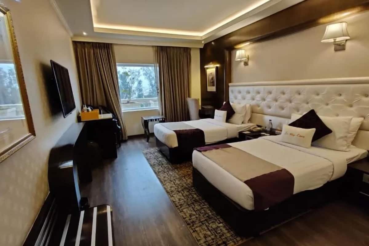 A hotel room with two beds, a desk, a TV, and a window with curtains.